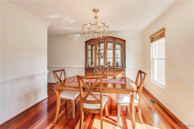 dining room featuring ornamental molding, hardwood / wood-style floors, visible vents, and a notable chandelier