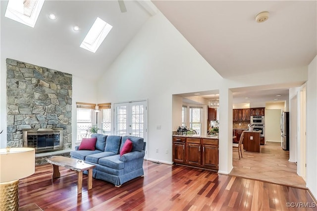 living room with high vaulted ceiling, a stone fireplace, a skylight, and wood finished floors