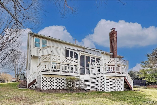 back of house featuring a deck, a sunroom, stairway, a lawn, and a trampoline