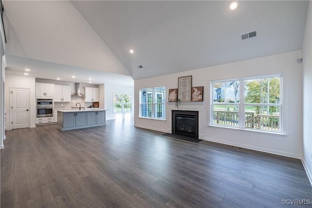 unfurnished living room featuring a glass covered fireplace, dark wood-type flooring, a sink, and visible vents