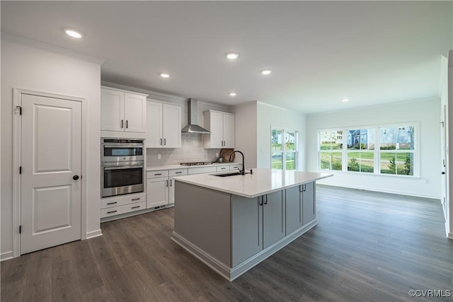 kitchen with tasteful backsplash, wall chimney exhaust hood, stainless steel appliances, crown molding, and a sink