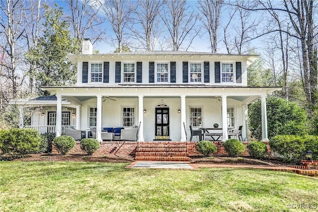 view of front facade featuring covered porch, a front yard, brick siding, ceiling fan, and a chimney