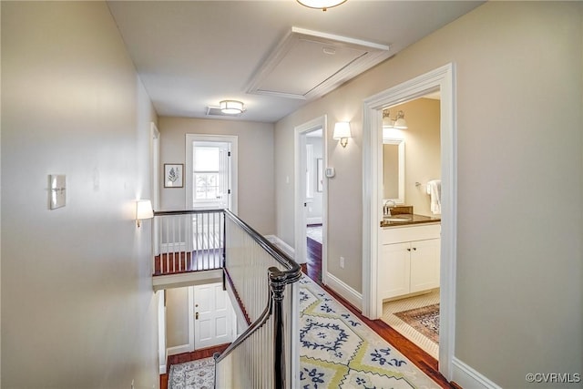 hallway featuring wood finished floors, baseboards, attic access, a sink, and an upstairs landing