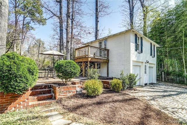 back of property featuring a deck, decorative driveway, brick siding, and an attached garage