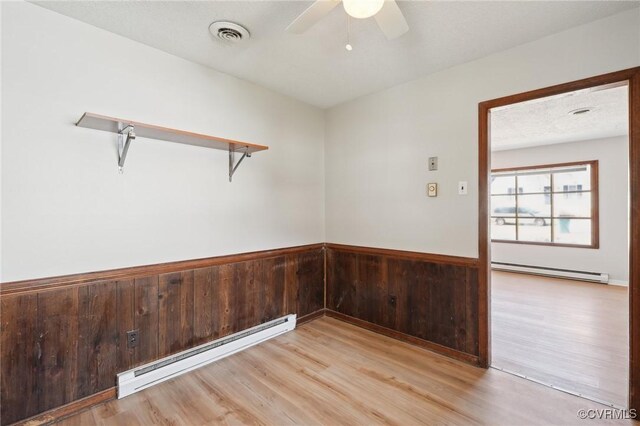 empty room featuring wainscoting, a baseboard radiator, visible vents, and light wood-style floors