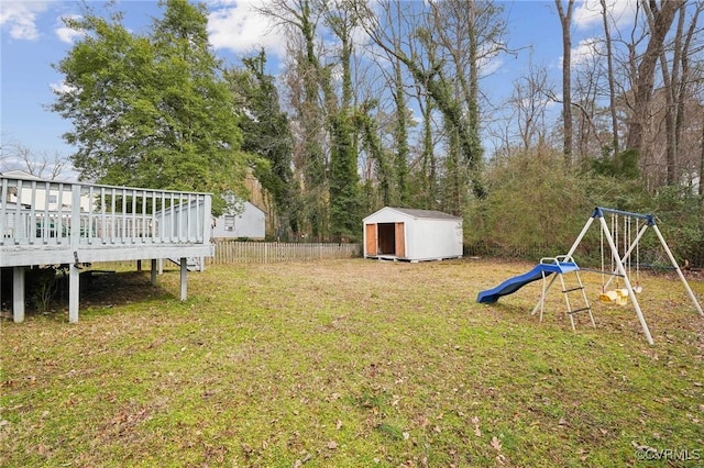 view of yard featuring an outbuilding, a playground, fence, a wooden deck, and a storage unit