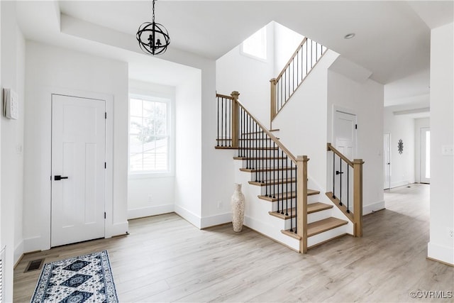 foyer entrance with a towering ceiling, stairway, light wood-style flooring, and baseboards