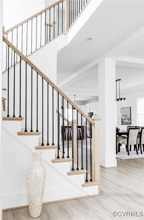 staircase with baseboards, a high ceiling, wood finished floors, and an inviting chandelier