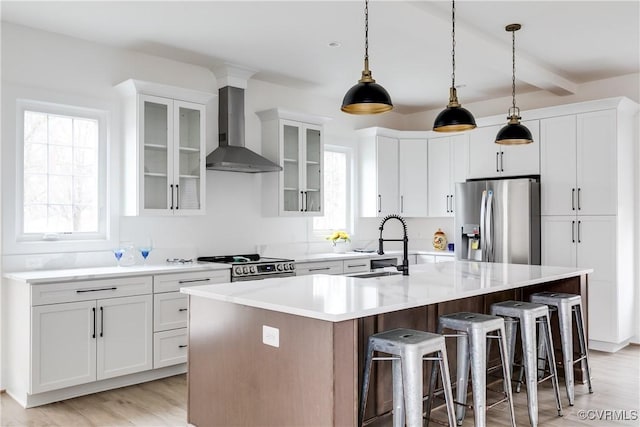 kitchen featuring a breakfast bar, stainless steel appliances, a kitchen island with sink, a sink, and wall chimney exhaust hood