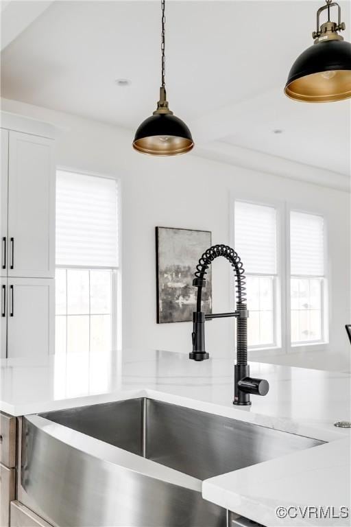 details with hanging light fixtures, white cabinetry, light countertops, and a sink