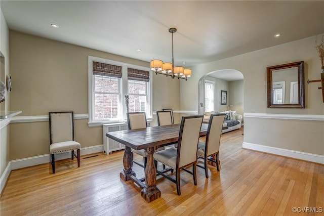 dining room with arched walkways, baseboards, light wood-style flooring, and radiator