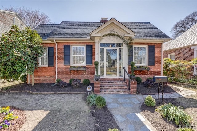 bungalow-style house featuring roof with shingles, brick siding, and a chimney