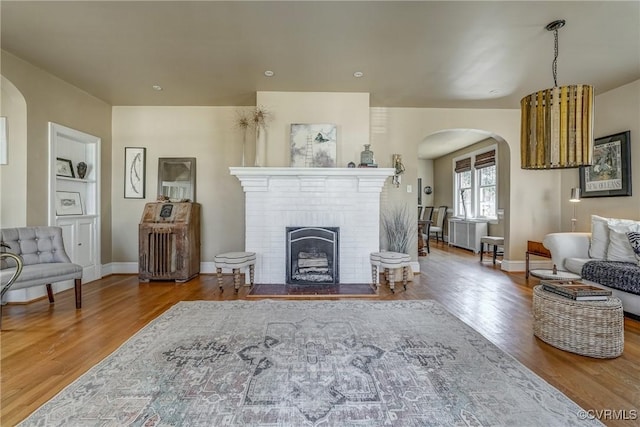 living room with arched walkways, a fireplace, baseboards, and wood finished floors