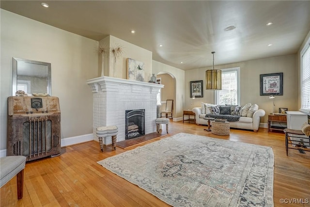 living area with arched walkways, recessed lighting, a brick fireplace, light wood-type flooring, and baseboards