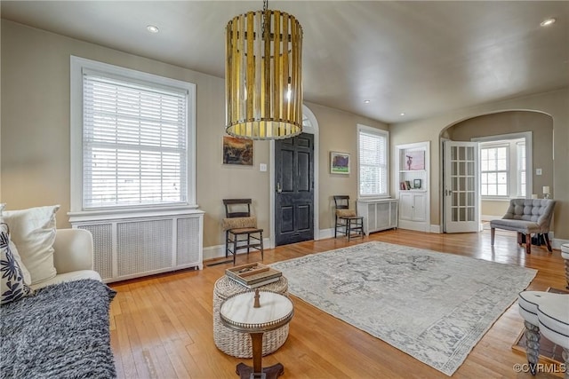 sitting room featuring hardwood / wood-style flooring, radiator heating unit, arched walkways, and a wealth of natural light