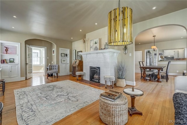 living area featuring light wood-type flooring, arched walkways, a brick fireplace, and recessed lighting