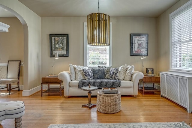 living area featuring arched walkways, radiator heating unit, light wood-style flooring, and baseboards