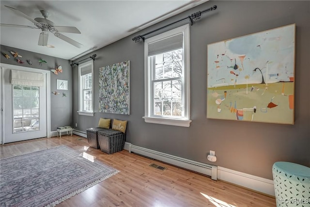 living area with a baseboard radiator, visible vents, a ceiling fan, wood finished floors, and baseboards