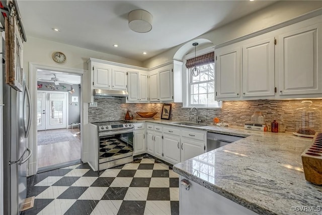 kitchen featuring under cabinet range hood, a sink, white cabinetry, appliances with stainless steel finishes, and light stone countertops