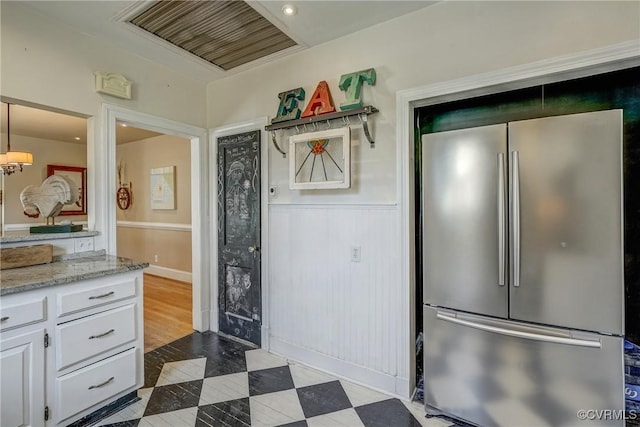 kitchen featuring visible vents, wainscoting, dark floors, freestanding refrigerator, and white cabinetry