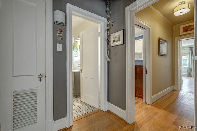 corridor featuring light wood-style floors, visible vents, baseboards, and ornamental molding