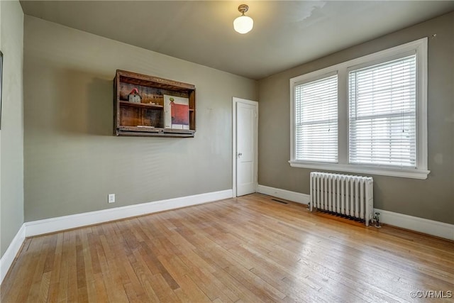 spare room featuring radiator, wood-type flooring, and baseboards