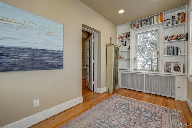 interior space featuring baseboards, built in shelves, wood finished floors, and radiator