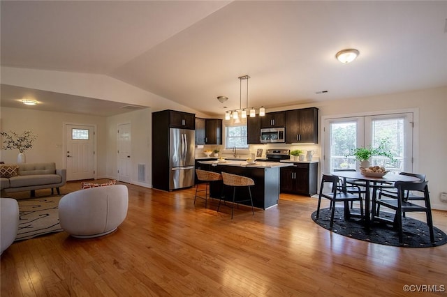 kitchen with wood finished floors, dark brown cabinetry, appliances with stainless steel finishes, open floor plan, and a center island