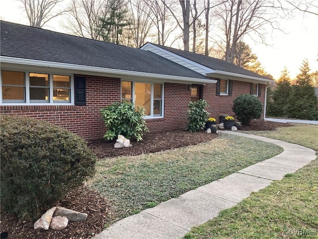 view of side of home with a yard, brick siding, and roof with shingles