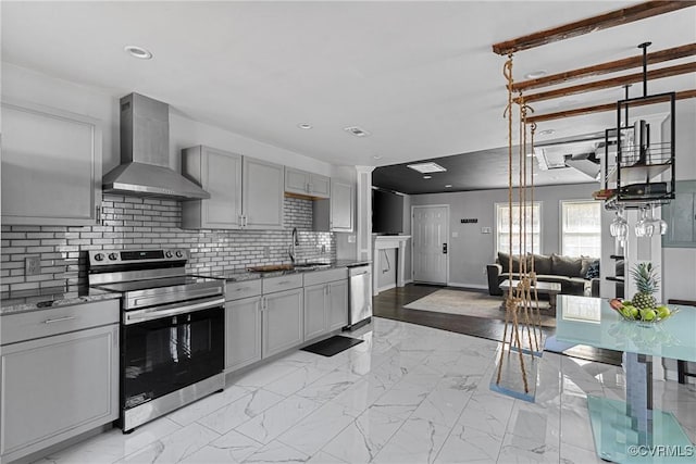 kitchen with wall chimney range hood, appliances with stainless steel finishes, marble finish floor, and a sink