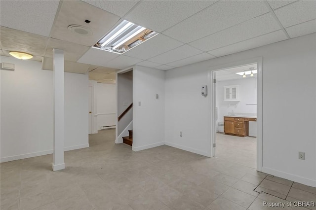 finished basement featuring stairway, a paneled ceiling, and baseboards