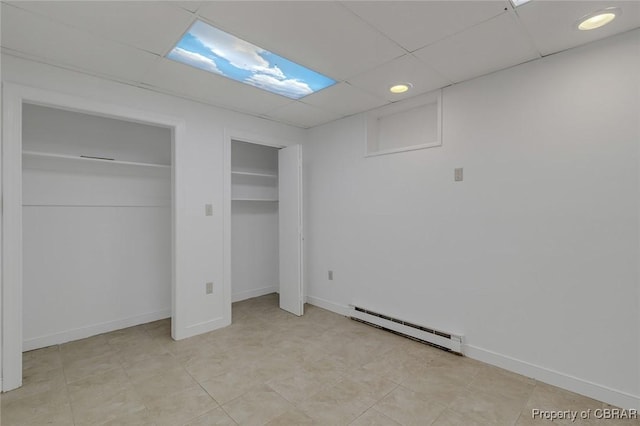 unfurnished bedroom with a baseboard heating unit, baseboards, a drop ceiling, and multiple closets