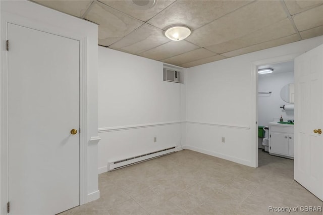 finished below grade area featuring a paneled ceiling, visible vents, a sink, and baseboard heating