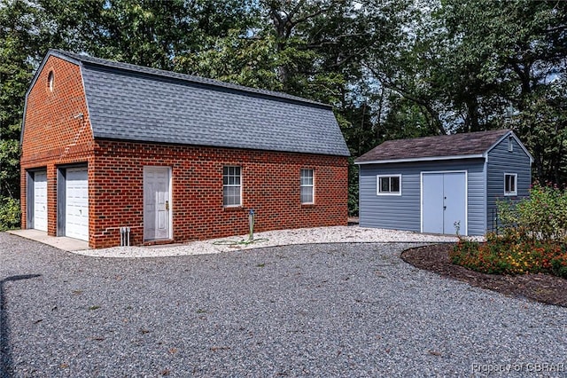 view of property exterior featuring an outbuilding, a garage, brick siding, a gambrel roof, and roof with shingles