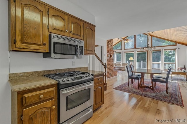 kitchen with stainless steel appliances, light wood-style flooring, brown cabinetry, vaulted ceiling, and brick wall