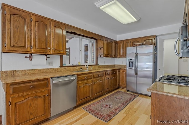 kitchen featuring a sink, light wood-style floors, light countertops, appliances with stainless steel finishes, and brown cabinetry