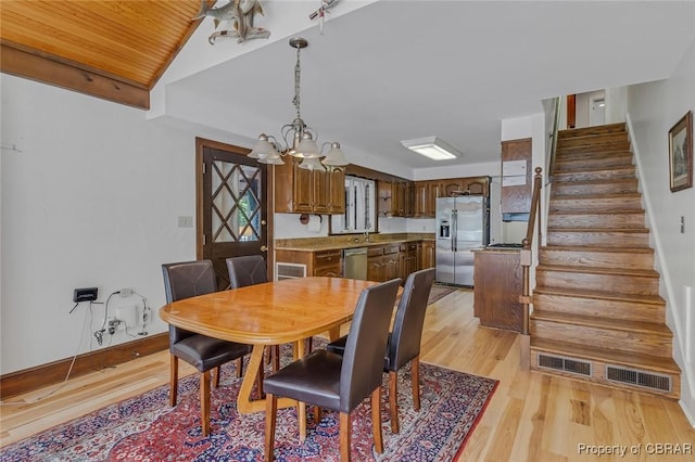 dining room featuring baseboards, stairs, vaulted ceiling, light wood-type flooring, and a notable chandelier