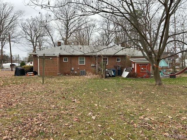 rear view of house with a chimney, brick siding, central AC unit, and a lawn