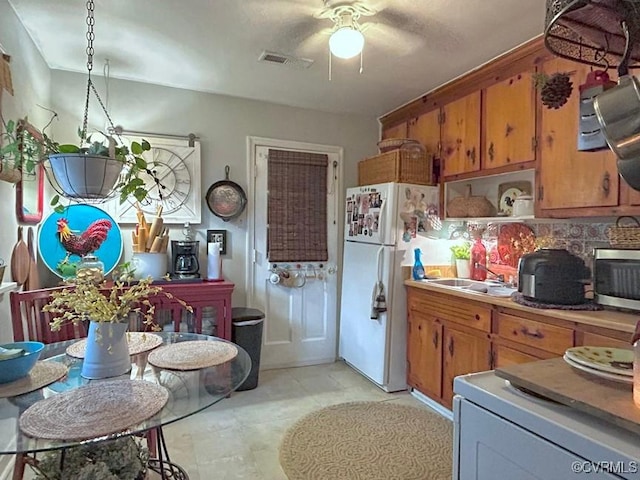 kitchen with stainless steel microwave, visible vents, ceiling fan, freestanding refrigerator, and brown cabinetry