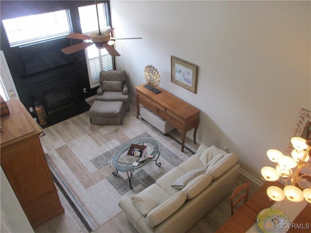 living room featuring ceiling fan with notable chandelier, a glass covered fireplace, and baseboards