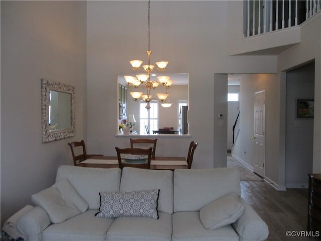 living area featuring a chandelier, baseboards, a high ceiling, and wood finished floors