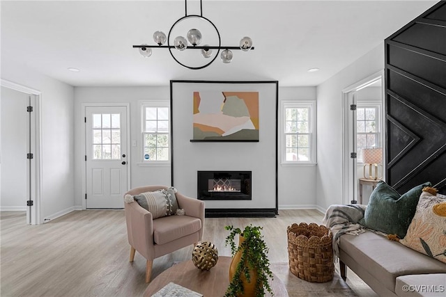 living area featuring light wood finished floors, a glass covered fireplace, and baseboards