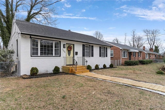 ranch-style house featuring a shingled roof, a front yard, brick siding, and fence