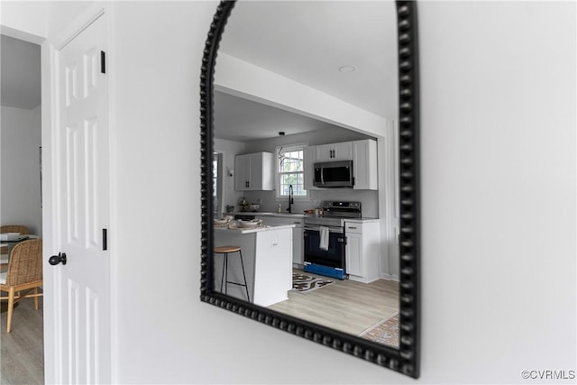 kitchen featuring white cabinets, stainless steel appliances, light countertops, light wood-type flooring, and a sink