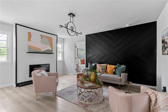 living room featuring visible vents, baseboards, a glass covered fireplace, an accent wall, and light wood-type flooring