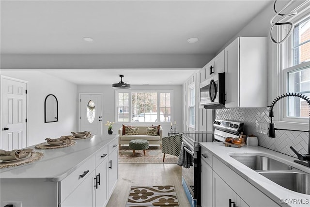 kitchen featuring white cabinets, light wood-style flooring, open floor plan, stainless steel appliances, and a sink