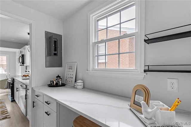 kitchen featuring white cabinetry, electric panel, black microwave, and light wood-style flooring