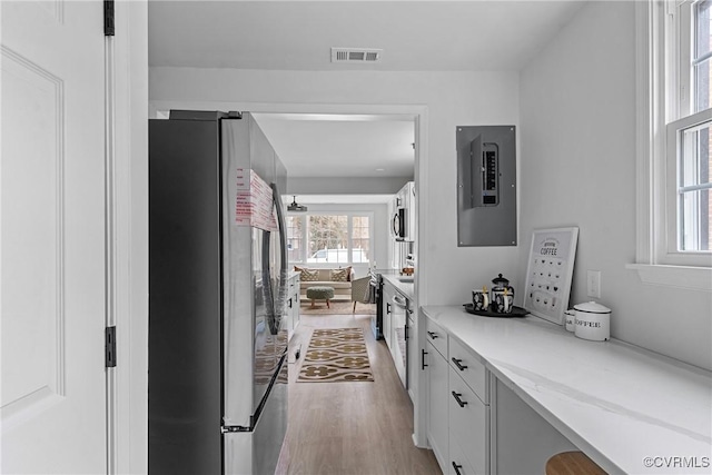 interior space with light wood-type flooring, freestanding refrigerator, electric panel, and visible vents