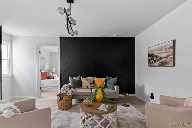 living area featuring an accent wall, wood finished floors, visible vents, and baseboards