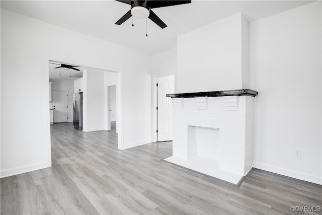 unfurnished living room with baseboards, a brick fireplace, a ceiling fan, and light wood-style floors